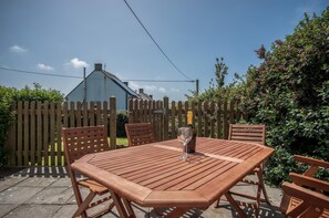 A wooden table and chairs set outdoors with a bottle of champagne on the table.