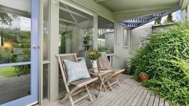 A covered outdoor seating area with two wooden chairs, a small table, and a potted plant.