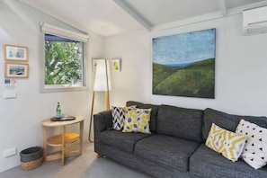 Uma sala de estar moderna com um sofá cinzento, uma mesa redonda pequena, uma luminária e uma grande pintura de paisagem na parede.