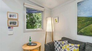 A room with a grey sofa, a small round table with a bottle, a lamp, and framed pictures on the wall.