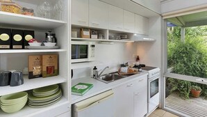 A modern kitchen with white cabinets, a microwave, a sink, and a window overlooking greenery.