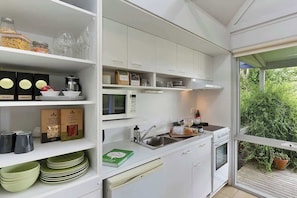 A modern kitchen with white cabinets, a microwave, a sink, and a window overlooking greenery.