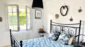 Un dormitorio con una cama, una mesita de noche, una lámpara y una ventana con un persiano abierto.