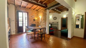 A rustic interior with a stone wall, wooden beams, a dining area with chairs, a fireplace, and a clock on the wall. - Panicale 7 - Three Bedroom Apartment, Sleeps 6 (Firenze)