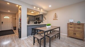 A modern kitchen with a dining area, featuring a wooden table and benches, a built-in microwave, and a small island with a plant. - Cozy Dog Friendly Retreat w/ Hot Tub & Views (Mchenry)