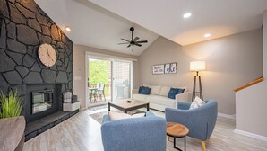 A modern living room with a stone fireplace, blue armchairs, a wooden coffee table, and a ceiling fan. - Cozy Dog Friendly Retreat w/ Hot Tub & Views (Mchenry)