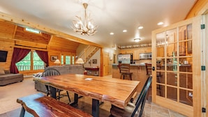 A spacious wooden interior with a large dining table, a kitchen area, and a staircase leading to an upper level. - Cozy Dog Friendly Cabin Near State Park w/ Hot Tub (Oakland)