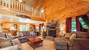 A spacious living room with a fireplace, high ceilings, and a balcony. - Cozy Dog Friendly Cabin Near State Park w/ Hot Tub (Oakland)