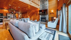 A spacious living area with a stone fireplace, wooden ceiling, and a balcony.