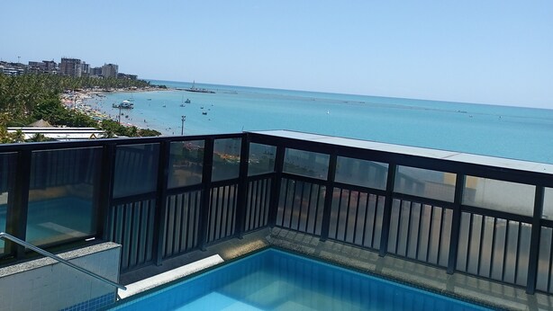 A swimming pool with a view of the beach and ocean. - Apartamento Beira Mar Pajuçara Maceió (Maceió)