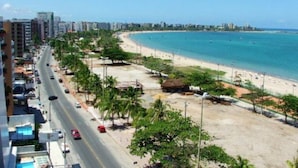A coastal road with a beach and high-rise buildings in the background. - Apartamento Beira Mar Pajuçara Maceió (Maceió)