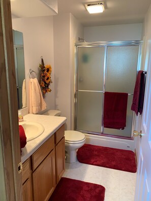 Ein Badezimmer mit Waschbecken, Toilette, Duschkabine aus Glas und roten Handtüchern.