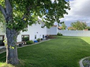 A residential property with a well-maintained lawn, a white fence, and a tree in the foreground. - Springtime in Montana - the Cottage is ready for your stay! (Billings)