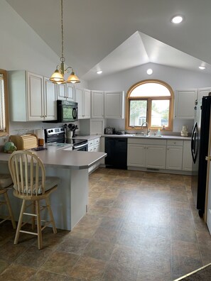A kitchen with white cabinets, a large island with a wooden chair, a microwave, stove, and a sink. - Springtime in Montana - the Cottage is ready for your stay! (Billings)