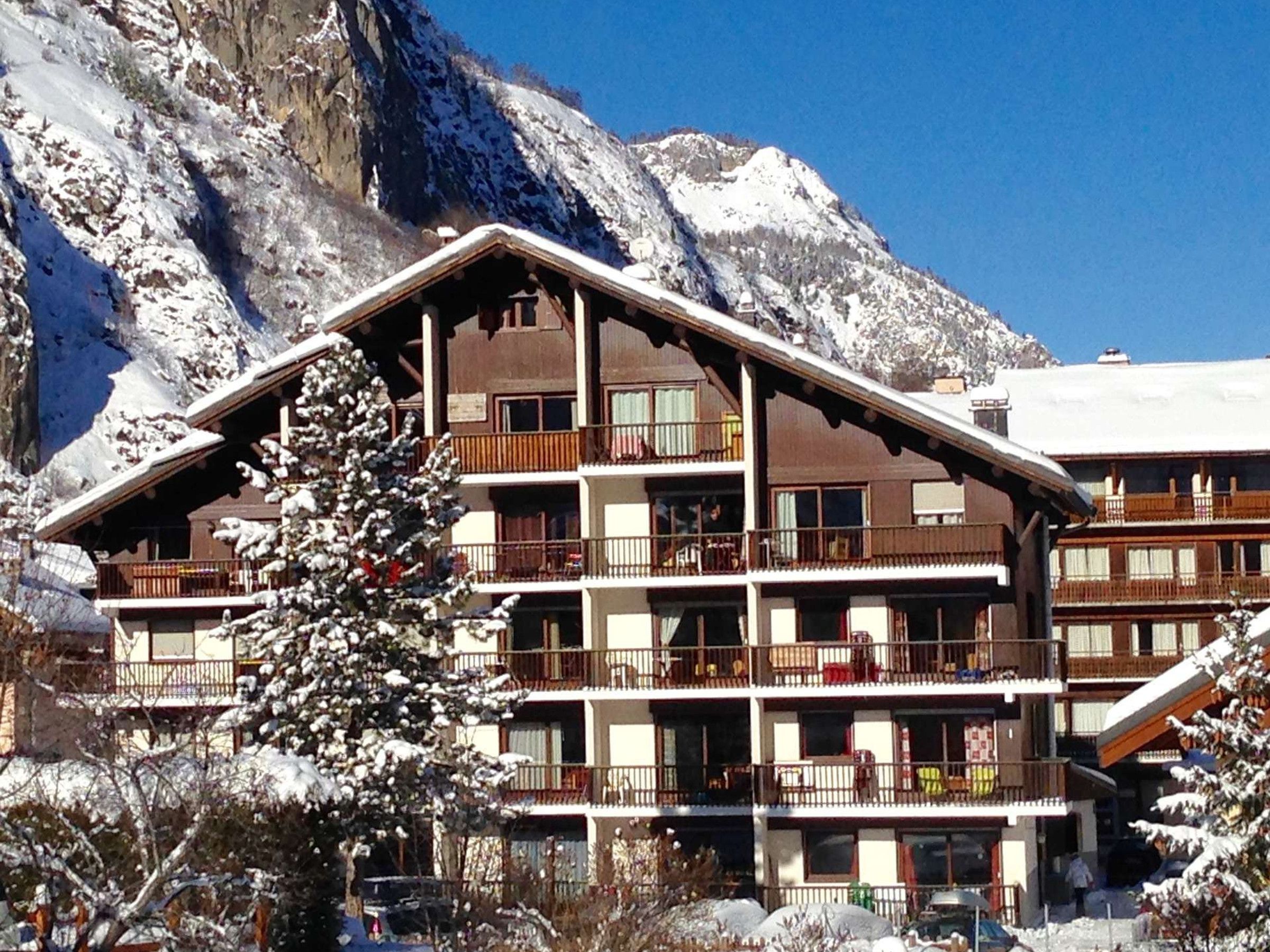 Un hotel amb balcons, situat davant d'un paisatge de muntanya nevada.