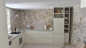 Eine kleine Küche mit weißen Schränken, einer Steinwand und einem Holzstuhl.