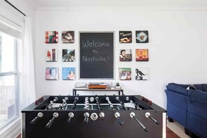 Une pièce avec une table de baby-foot, un canapé bleu et un mur orné de tableaux et d’un panneau noir.
