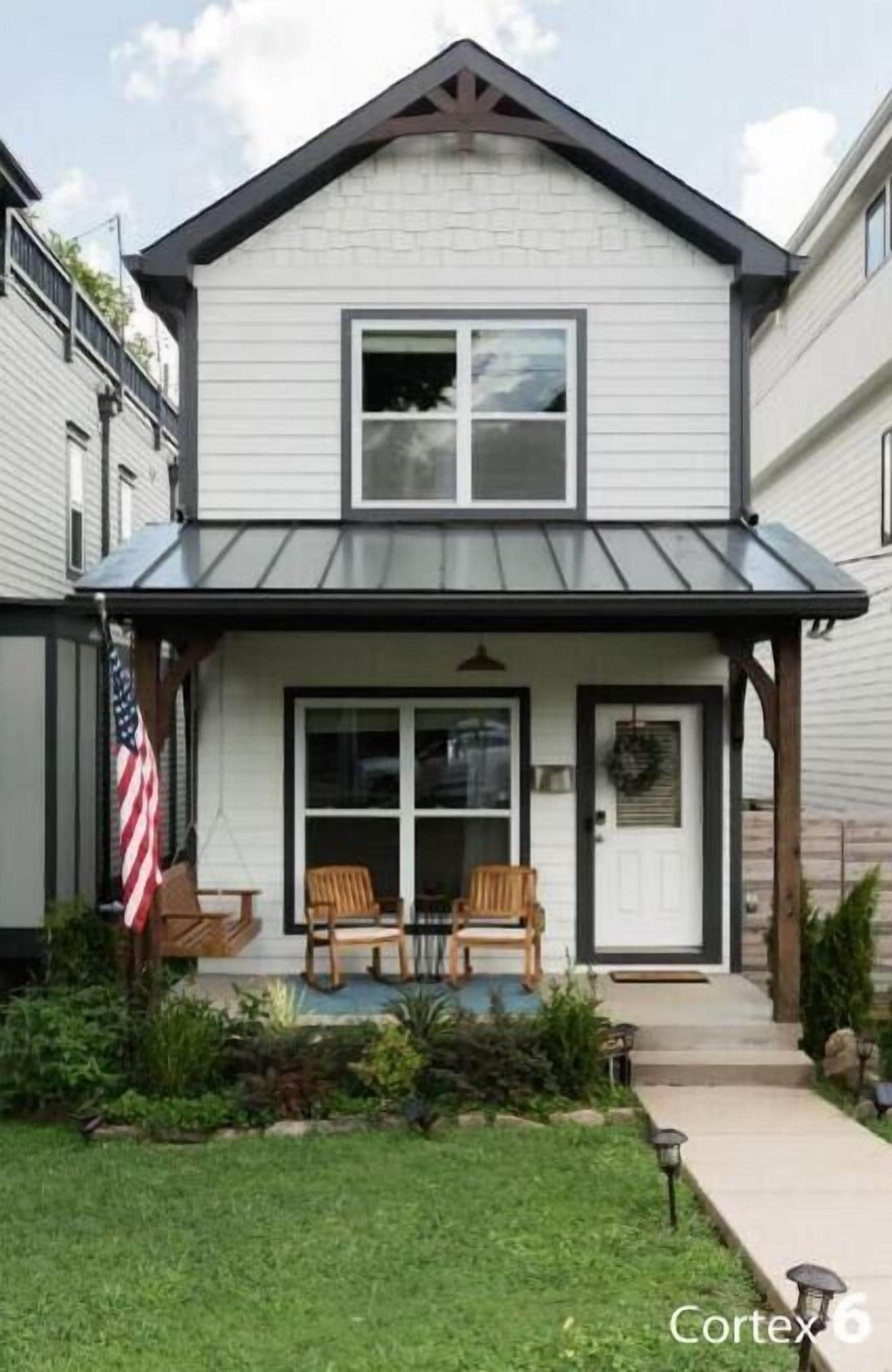 A two-story house with a front porch, a small garden, and an American flag.