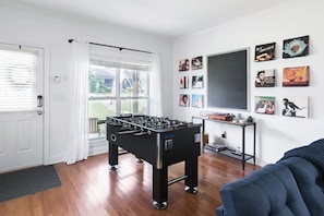 A room with a foosball table, a TV, and various framed pictures on the wall.