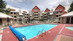 A swimming pool with lounge chairs and umbrellas, surrounded by multi-story buildings with a red and grey color scheme. - Lake Placid Lodge by Whistler Premier (Whistler)