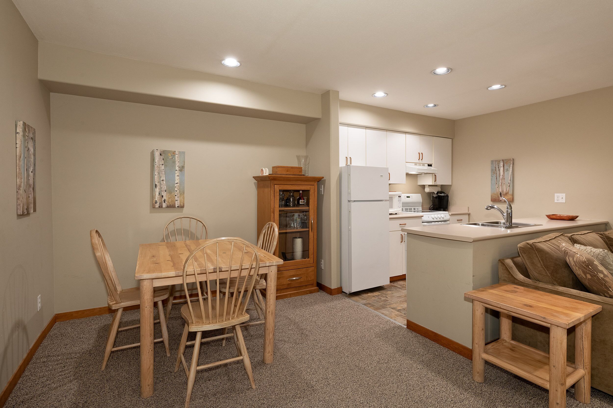 A compact kitchen with wooden cabinetry, a dining table with chairs, and a small wooden stool.