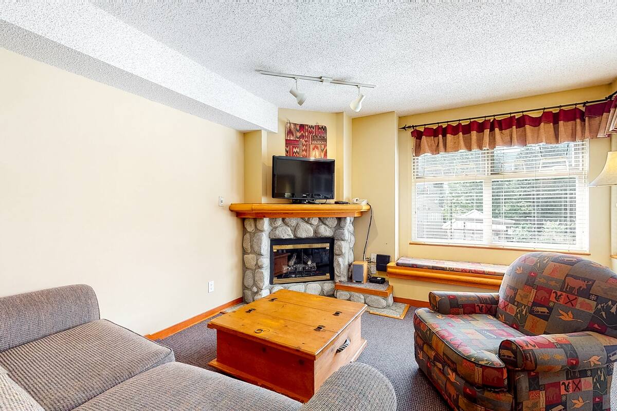 A living room with a stone fireplace, a television, a patterned armchair, and a wooden coffee table.