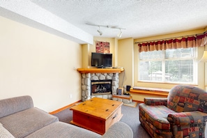 A living room with a stone fireplace, a television, a patterned armchair, and a wooden coffee table.