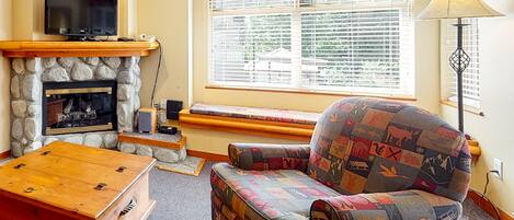 A cozy living room with a stone fireplace, a comfortable armchair, a wooden coffee table, and a television on a mantel.