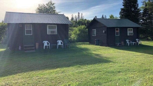 Deux petites cabanes aux toits métalliques, entourées d’herbe et d’arbres.