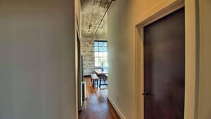 A hallway leading to a dining area with exposed brick walls, a wooden floor, and a large window. - Gorgeous Ultramodern 2BR Corner Loft + Workspace (Saint Louis)