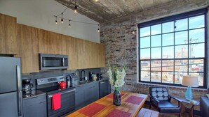 A modern kitchen with a large window, a dining area with a wooden table, and a brick wall. - Gorgeous Ultramodern 2BR Corner Loft + Workspace (Saint Louis)