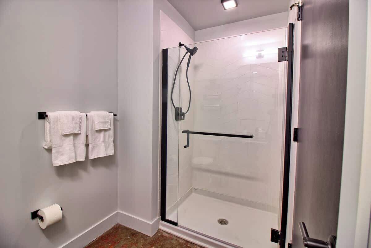 A modern bathroom with a glass-enclosed shower, a towel rack with towels, and a toilet paper holder.
