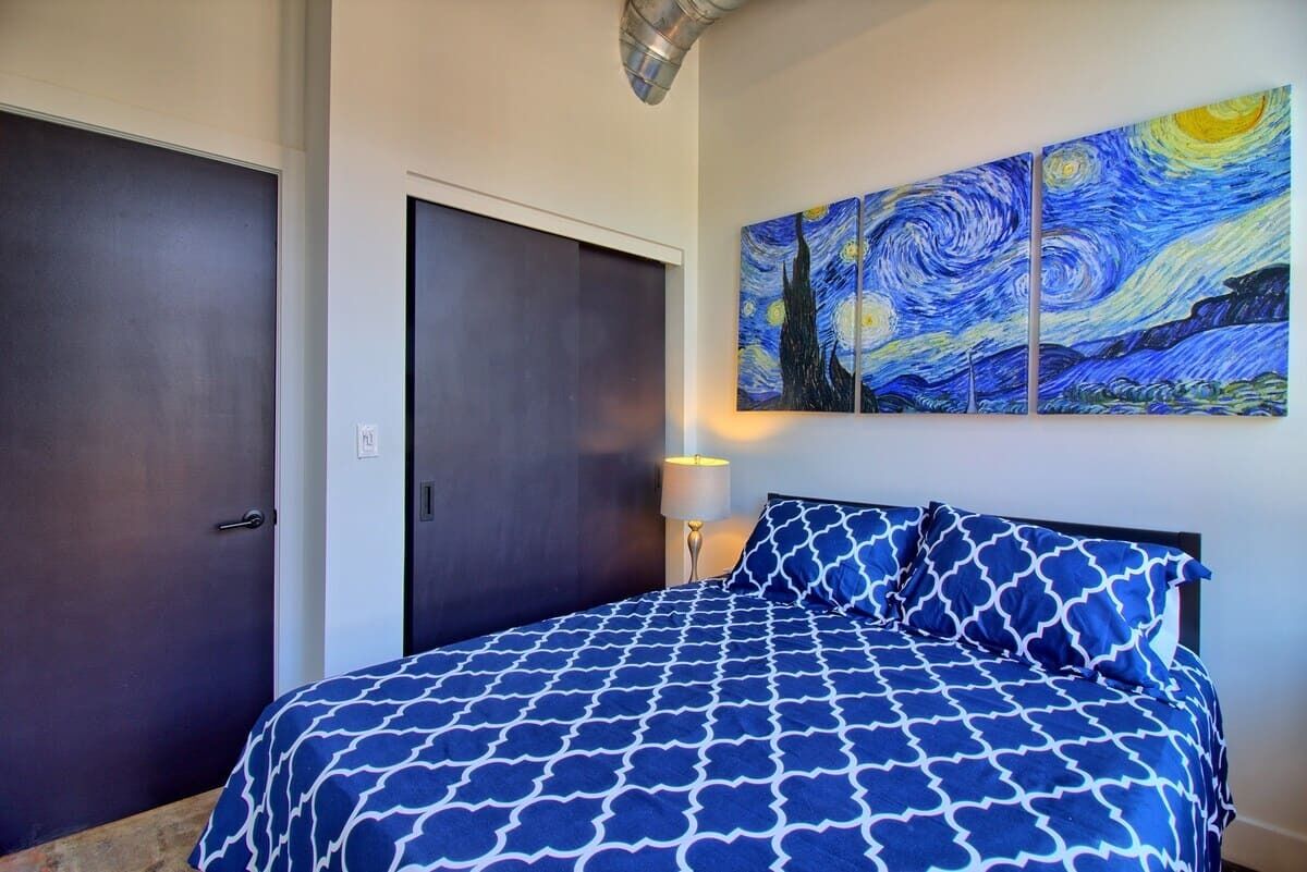 A bedroom with a bed, a nightstand, a lamp, and a painting on the wall.