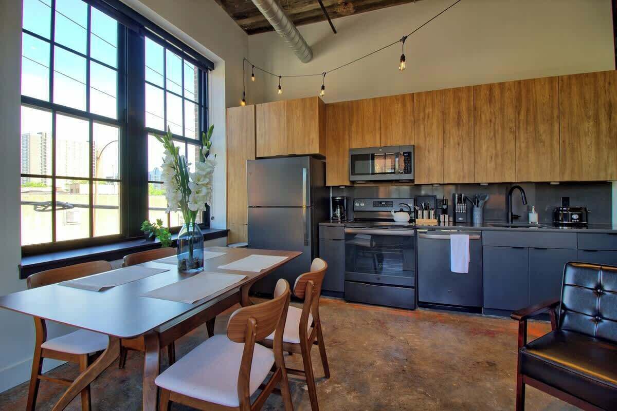 A modern kitchen with wooden cabinets, stainless steel appliances, and a dining area with a table and chairs.