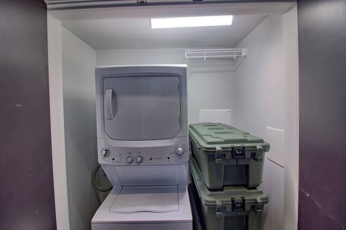 A compact room with a washing machine, a small shelf, and two green storage bins.
