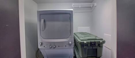 A compact room with a washing machine, a small shelf, and two green storage bins.