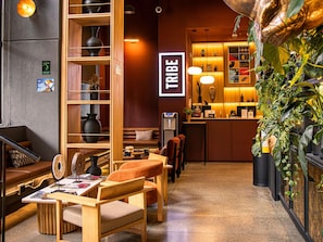 Un espace salon accueillant, doté de meubles en bois, d’un comptoir de réception et d’une enseigne murale portant l’inscription « TRIBE ».