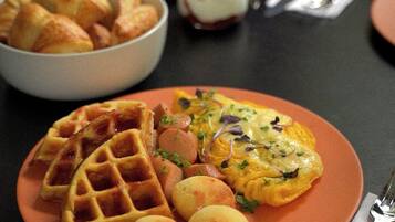 A plate with waffles, eggs, and small round items, possibly cheese or potatoes, on a table.