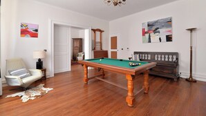 Une pièce comprenant une table de billard, un canapé, un fauteuil, une lampe et des œuvres d’art accrochées aux murs.