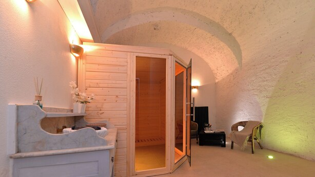 Une pièce chaleureuse avec un sauna en bois, un banc en marbre blanc et une petite table sur laquelle est posé un vase de fleurs.