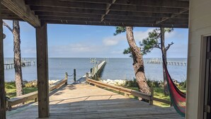 A wooden deck leading to a beach with a hammock and a view of the ocean and piers. - Private Bayfront Apartment with King bed and Awesome View (Saint George Island)