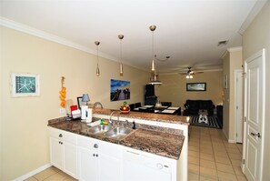 Enjoy meals in the well-equipped kitchen with a central island and double sink, adjacent to a dining area with a table and chairs.