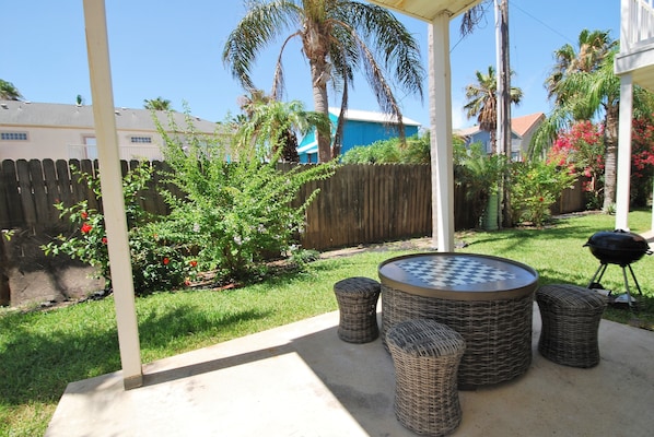 Relax in a serene outdoor space surrounded by lush greenery and a barbecue grill.