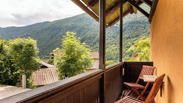 Ein Balkon mit Holzbalkonen, zwei Holzstühlen und Blick auf ein bewaldetes Gebirge.