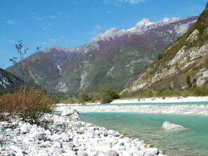 Une rive rocheuse bordant une rivière aux eaux turquoise et limpides, entourée de montagnes et d’une végétation clairsemée.