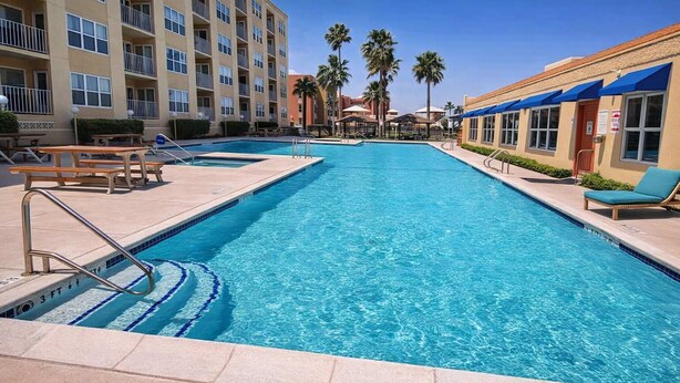 Une piscine dont la profondeur est indiquée à 3 pieds, des chaises longues et un bâtiment doté de balcons.