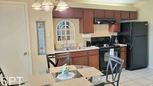 Une cuisine avec des meubles de rangement en bois, un réfrigérateur noir, une cuisinière et une table à manger avec des chaises.