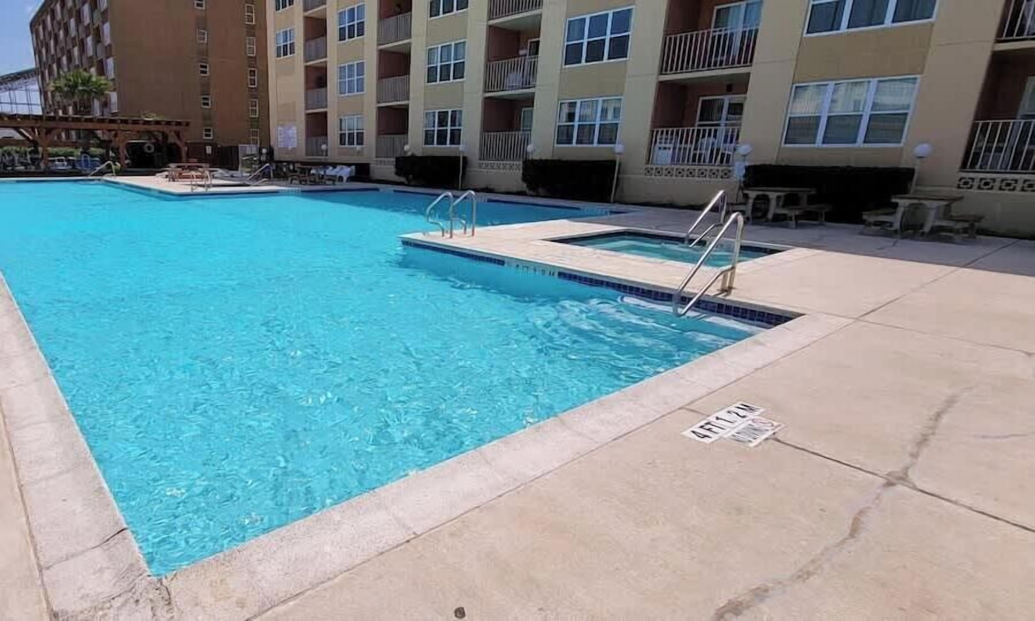 A swimming pool with a concrete deck, surrounded by a multi-story building with balconies.
