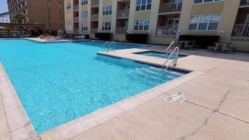 A swimming pool with a concrete deck, surrounded by a multi-story building with balconies.