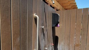 Une terrasse en bois, dotée d’une rambarde métallique et d’une petite boîte noire, vraisemblablement un haut-parleur, fixée au mur.